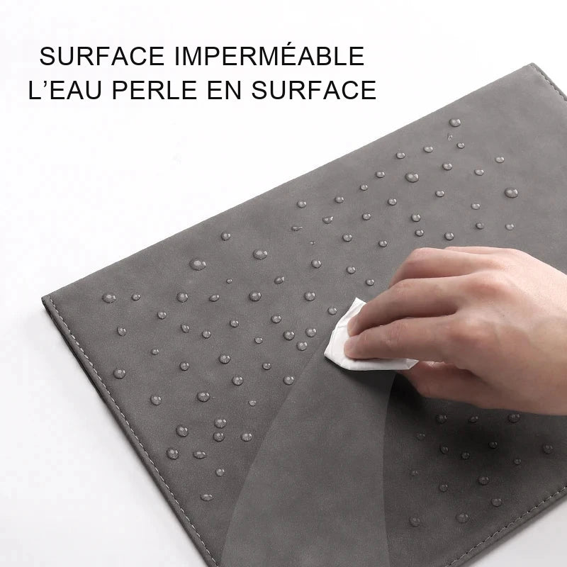 Gouttes d'eau perlant à la surface d'une housse d'ordinateur grise qu'une main essuie avec un mouchoir en papier.
