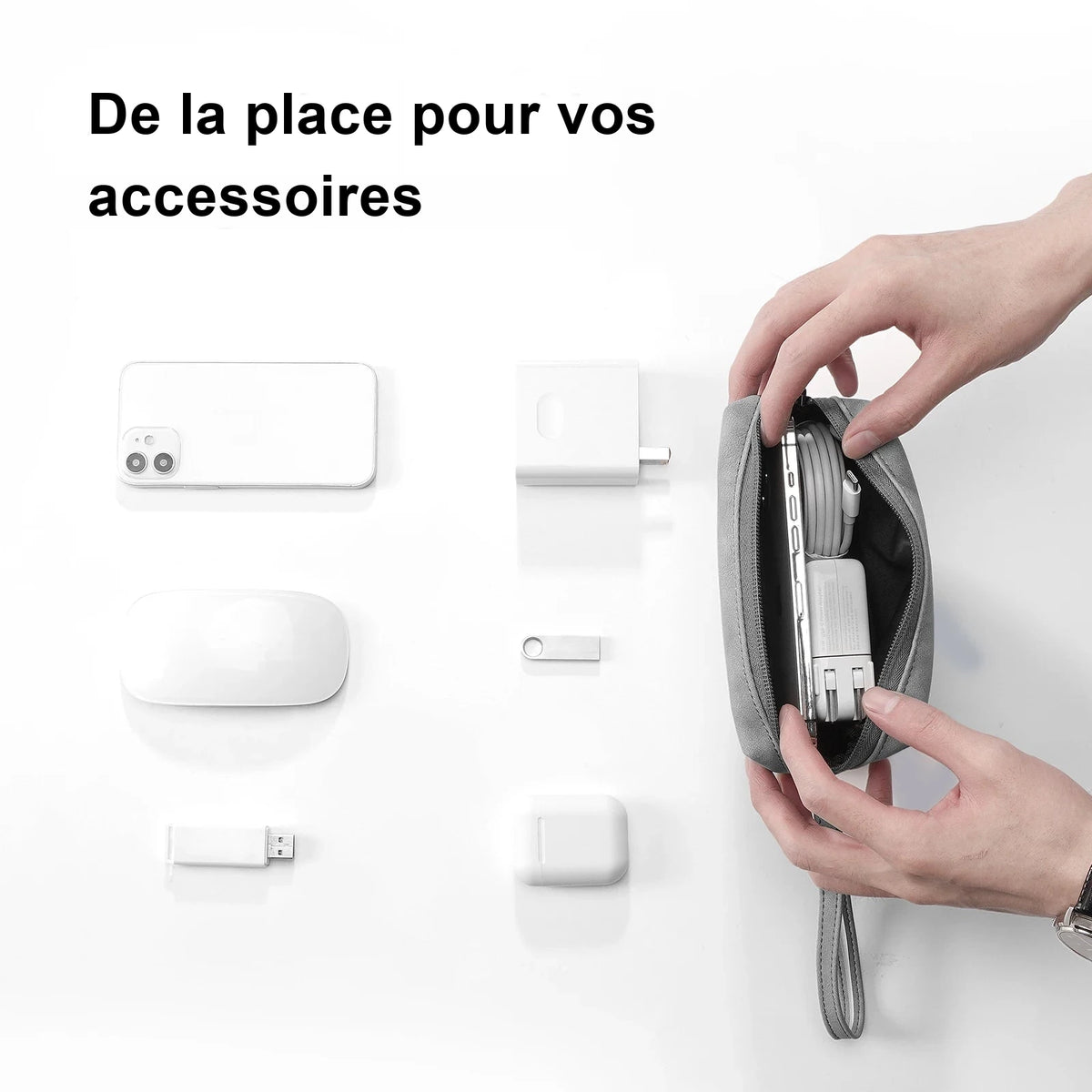 Deux mains ouvrent une trousse d'accessoires grise contenant un chargeur et un câble, entourée d'un téléphone, d'une souris et de clés USB.