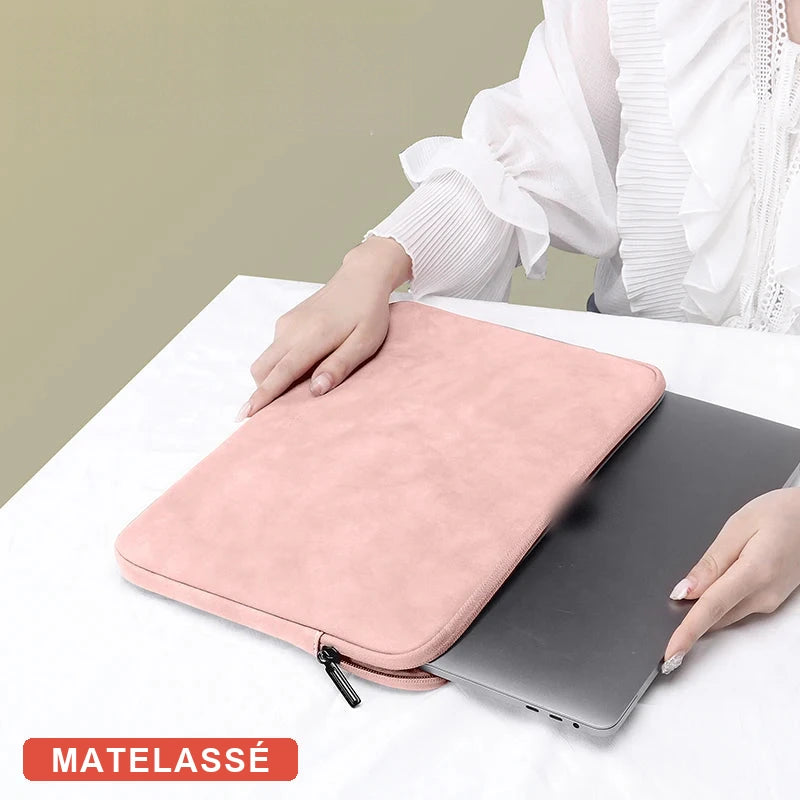 Pochette rose matelassée pour ordinateur portable posée sur un ordinateur portable gris foncé entrouvert, mains d'une personne en haut à droite, avec le badge MATELASSÉ.