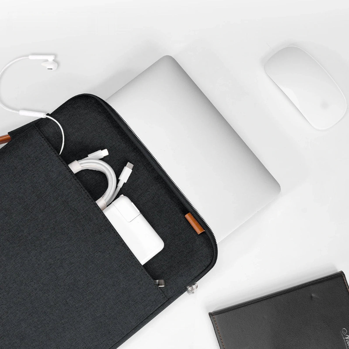 Housse en tissu noir posée sur un bureau blanc, poche avant contenant un câble et un chargeur, à côté d'un ordinateur portable et d'une souris.