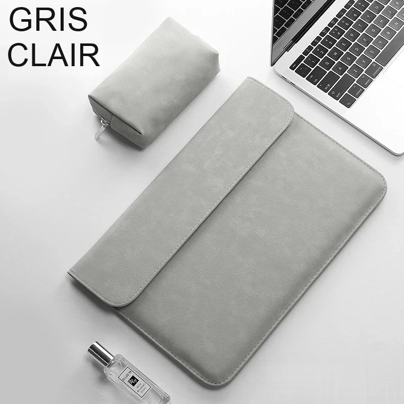 Pochette ordinateur gris clair en simili cuir, rabat fermé, posée en biais sur un bureau avec sa trousse assortie et un ordinateur portable.