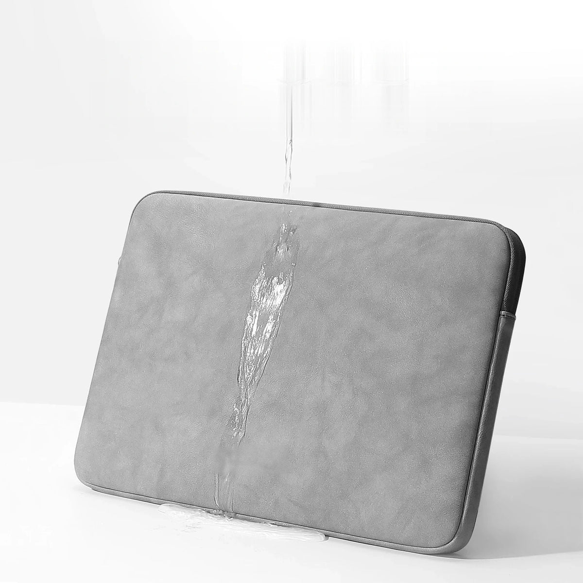 Pochette ordinateur grise en simili cuir texturé, posée en biais, avec un filet d'eau qui ruisselle sur sa face imperméable.