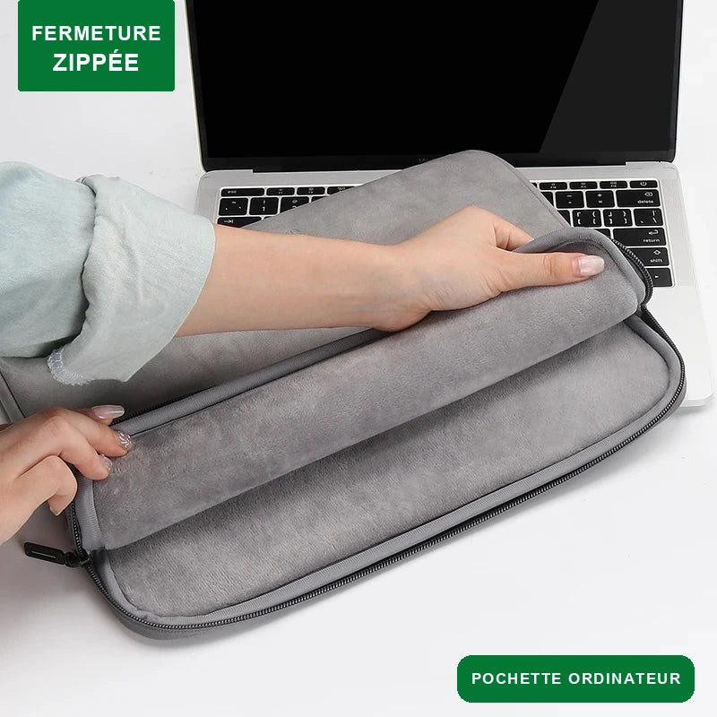 Pochette ordinateur grise à fermeture zippée, tenue ouverte à deux mains devant un ordinateur portable.