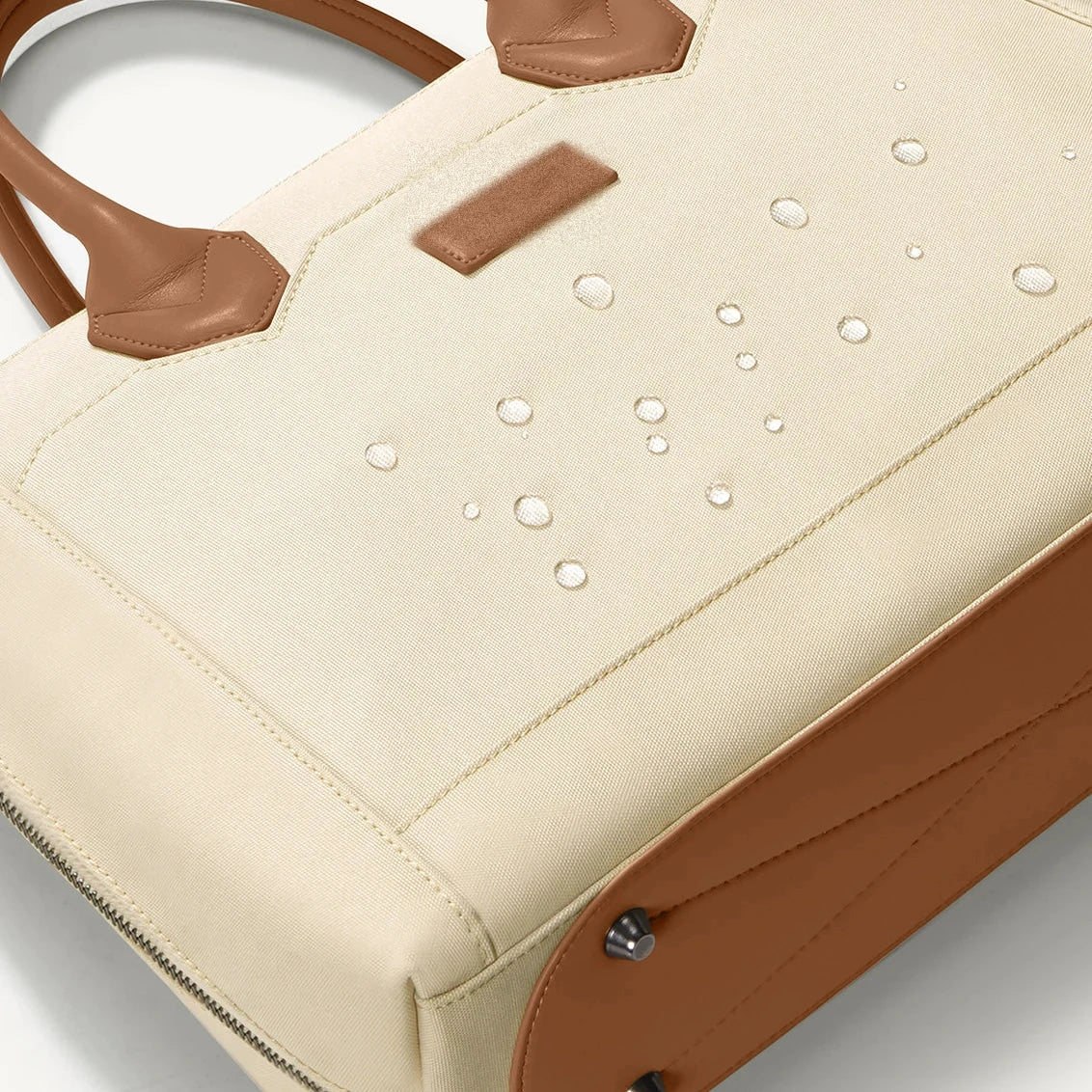 Sac cabas en toile écrue avec anses, soufflets et étiquette en cuir fauve, gouttes d'eau perlant sur le tissu déperlant.