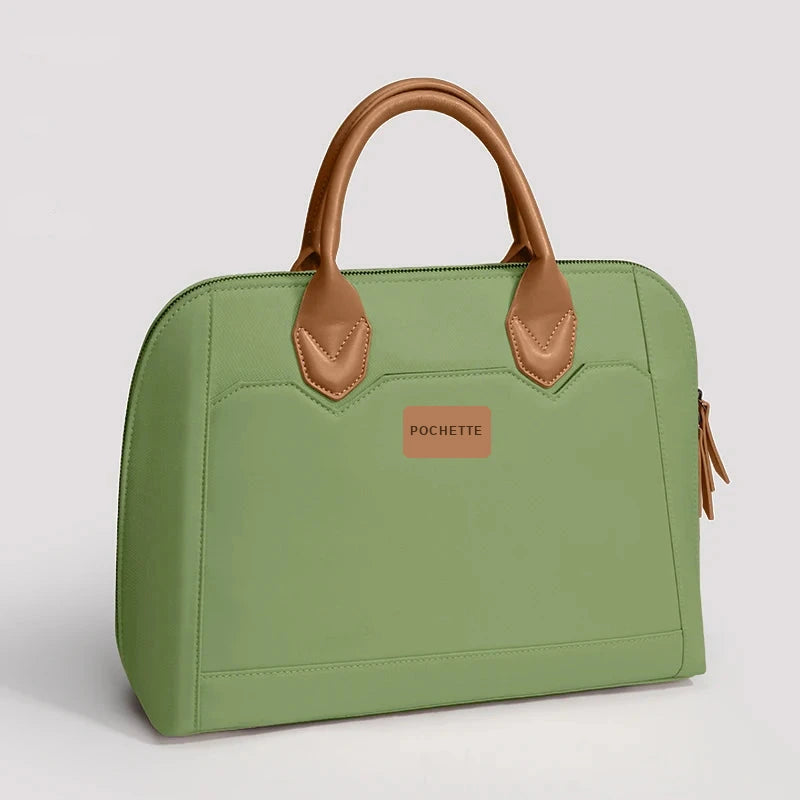 Sac cabas pour ordinateur portable en cuir vert sauge avec anses et empiècements en cuir cognac, étiquette rectangulaire sur la face avant.