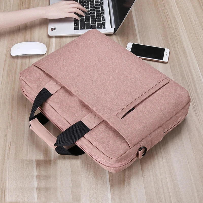 Sacoche ordinateur rose posée en biais sur un bureau en bois, poignée noire rabattue et poche zippée visible sur le dessus.