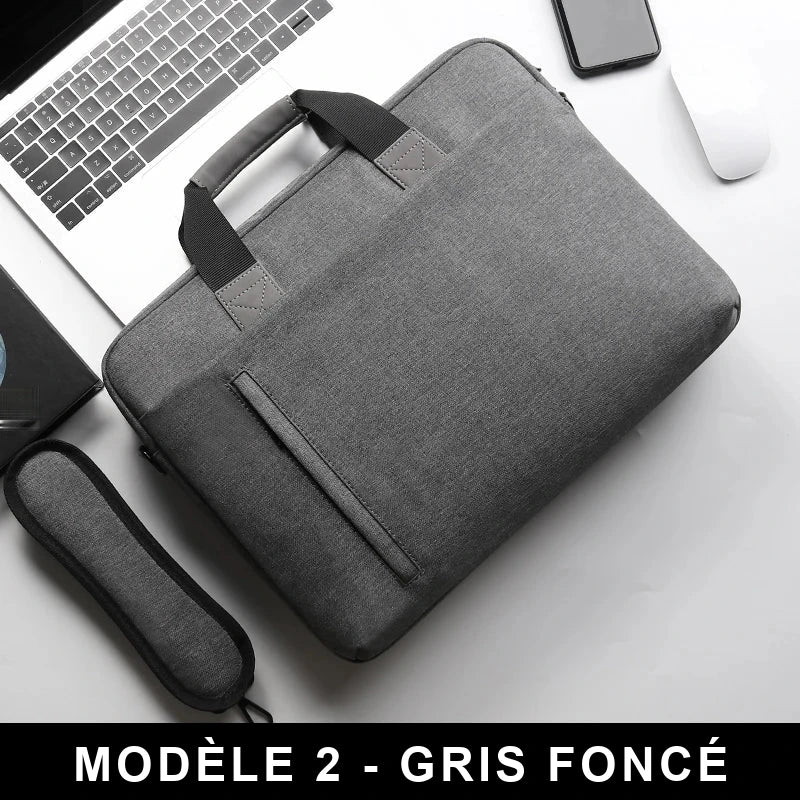 Sacoche pour ordinateur portable gris foncé avec poignée matelassée et bandoulière assortie, posée sur un bureau à côté d'un clavier, d'un smartphone et d'une souris.