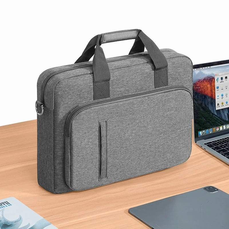 Sacoche en toile grise pour ordinateur portable, posée de trois quarts sur un bureau en bois à côté d'un ordinateur ouvert.