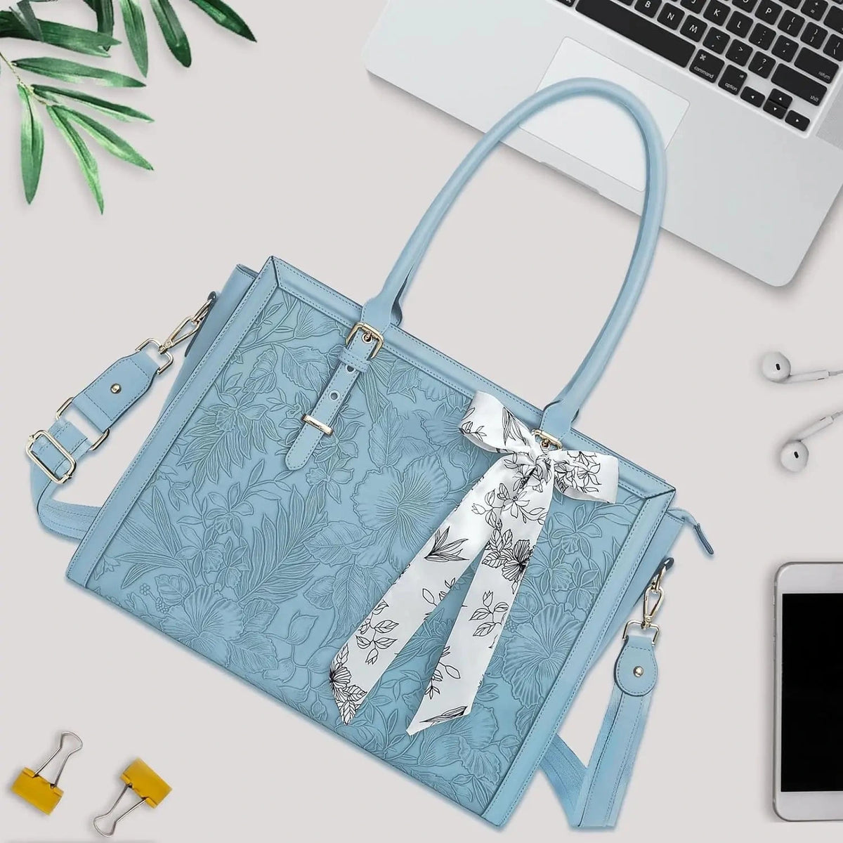 Grand sac cabas bleu clair en simili cuir gaufré à motif floral, posé à plat près d'un ordinateur portable, avec foulard noué et bandoulière amovible.