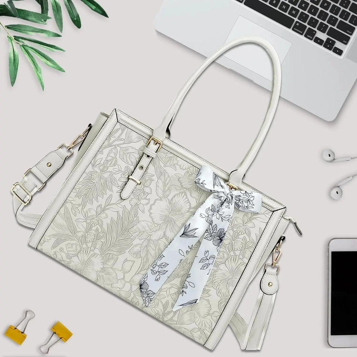 Sac ordinateur blanc cassé posé à plat sur un bureau, en biais, entre un ordinateur portable, des écouteurs et un téléphone.