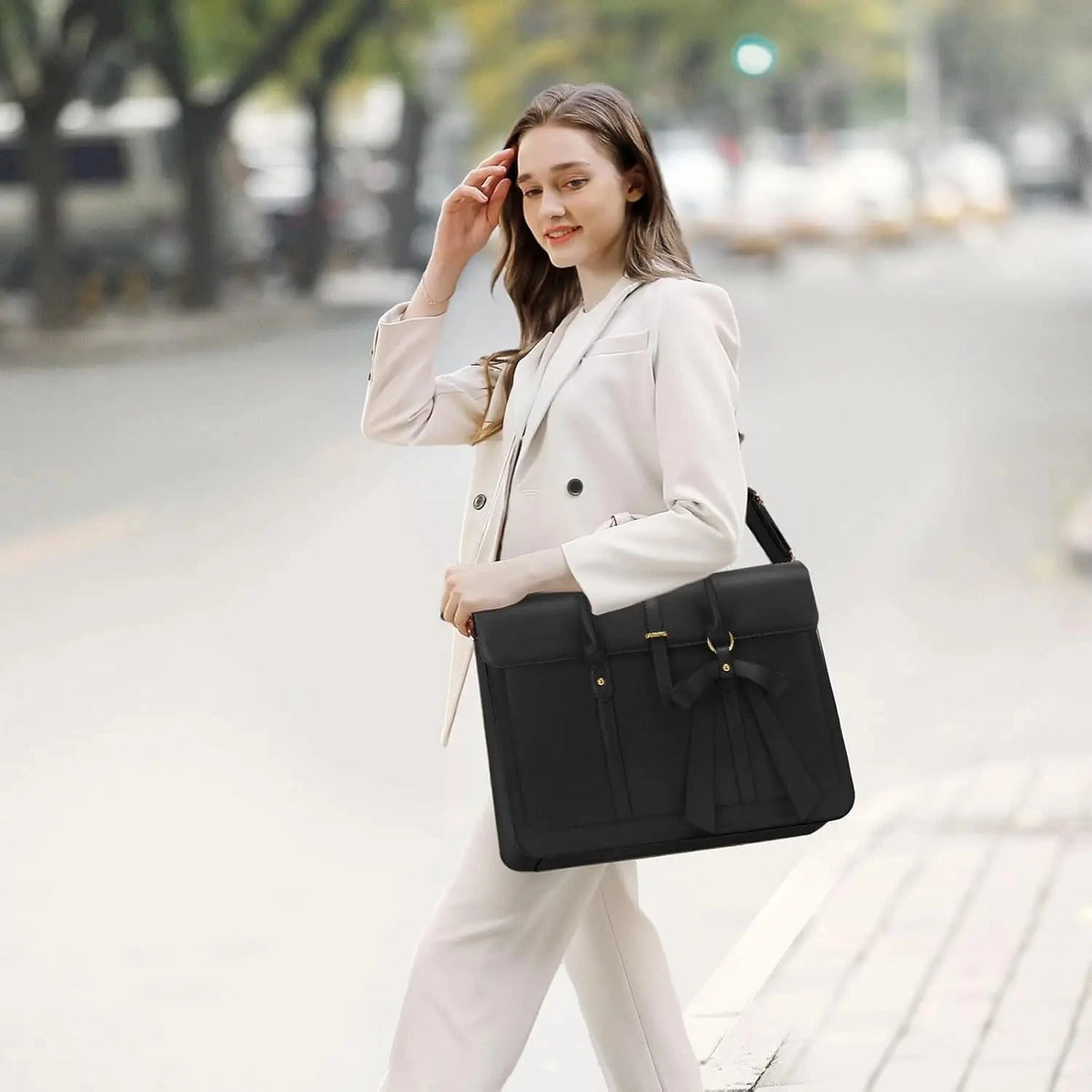 Femme en tailleur clair marchant en ville, le sac cartable noir porté à la main.