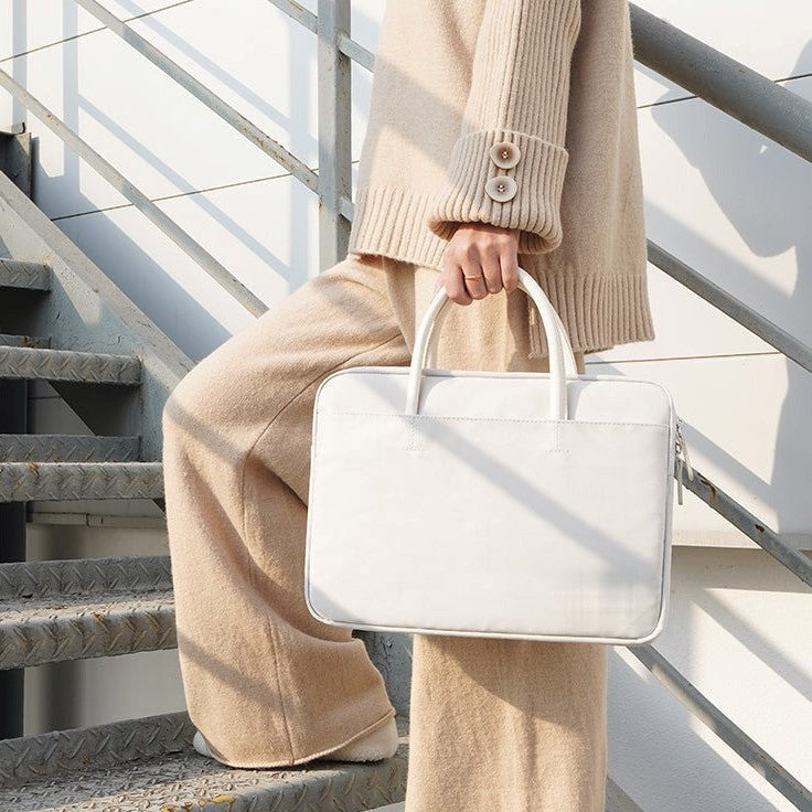Sacoche blanche pour ordinateur portable 14 pouces, tenue par sa poignée dans un escalier extérieur.