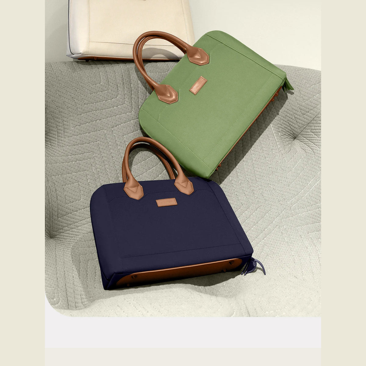 Deux sacoches pour ordinateur portable, une verte et une bleu marine, posées sur un couvre-lit matelassé clair, une troisième sacoche crème à l'arrière-plan.