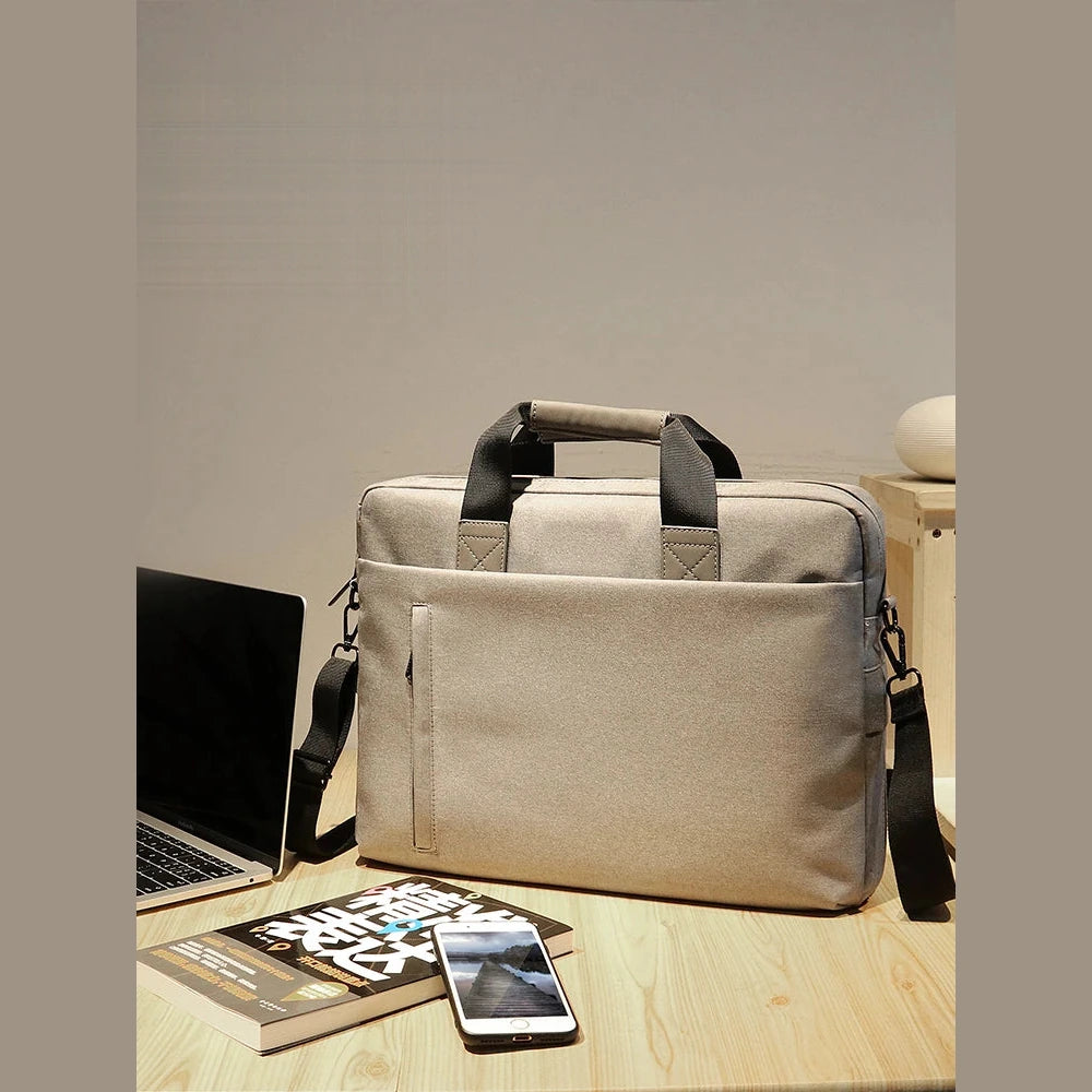 Sacoche pour ordinateur portable en toile beige, posée sur un bureau en bois à côté d'un ordinateur ouvert.