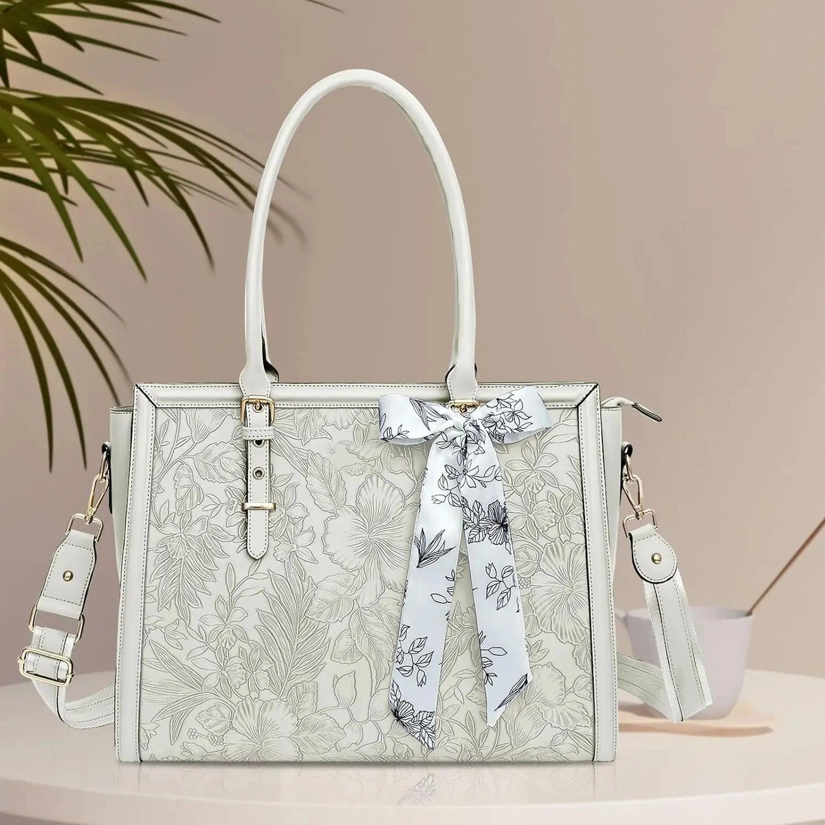 Sac ordinateur blanc cassé en simili cuir gaufré à motif floral, vu de face avec son foulard imprimé noué sur l'anse.