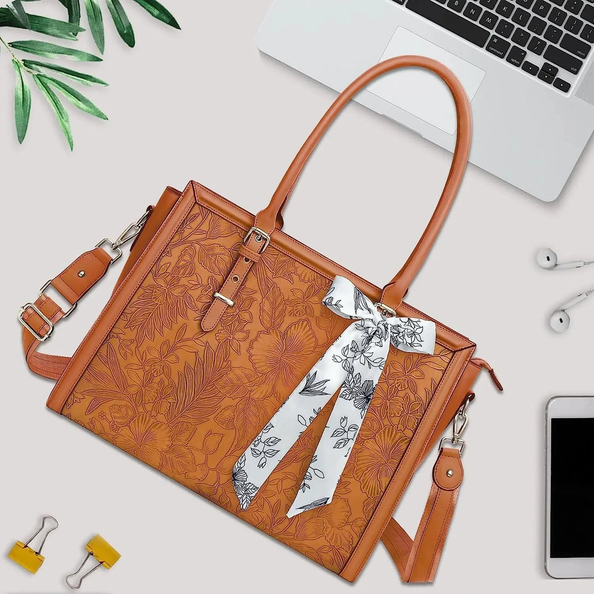 Grand sac cabas en cuir camel gaufré de motifs floraux, foulard blanc noué à l'anse, posé sur un bureau avec un ordinateur portable.