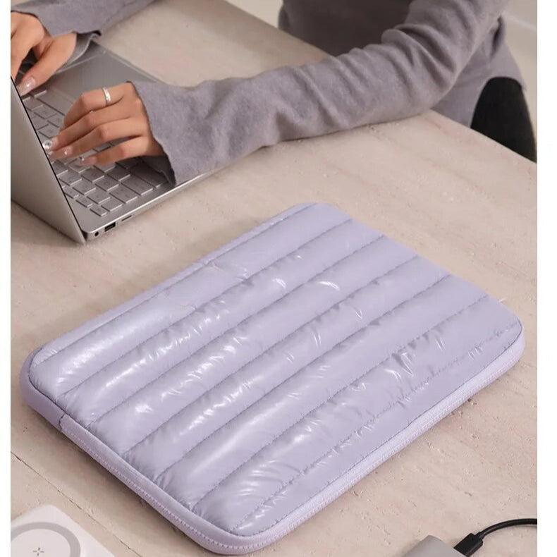 Housse matelassée lilas posée sur un bureau clair, vue de trois quarts, à côté d'un ordinateur portable ouvert.