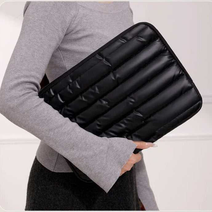 Femme portant sous le bras une housse matelassée noire pour ordinateur portable, vue de trois quarts.