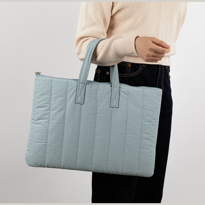 Sac ordinateur matelassé bleu ciel porté à la main le long du corps, anses courtes et coutures verticales.