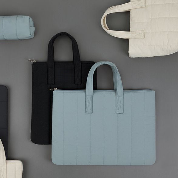 Vue à plat de la gamme sur fond gris : trousse et sacoche bleu ciel, sacoche noire et sac fourre-tout écru.
