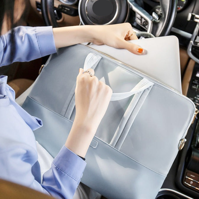 Sac ordinateur bleu clair tenu à la main dans une voiture, gros plan sur la poignée blanche et la fermeture éclair