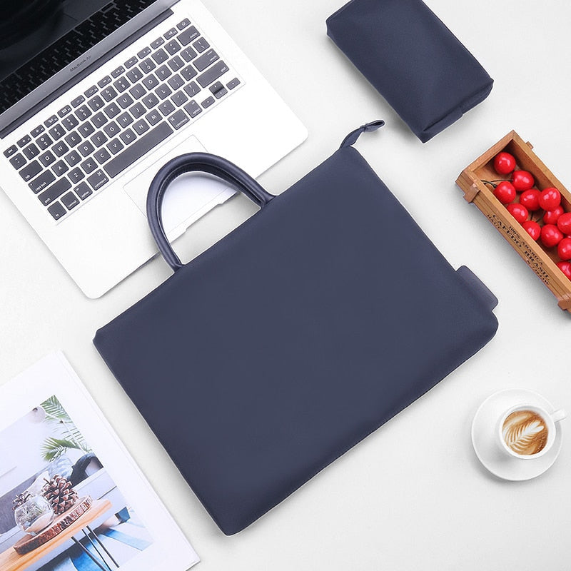 Sacoche bleu marine pour ordinateur portable posée à plat, avec ordinateur ouvert, pochette assortie, cagette de cerises et tasse de café.