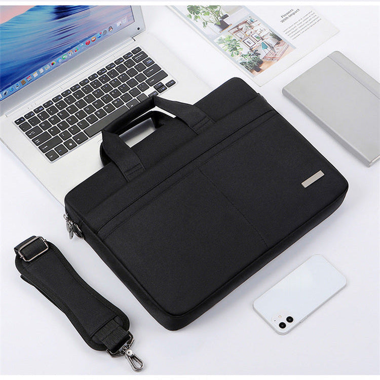 Sacoche noire en toile pour ordinateur portable 17 pouces, poignée rembourrée et poche zippée à l'avant, bandoulière détachée posée à gauche, sur un bureau blanc avec un ordinateur portable ouvert et un magazine.