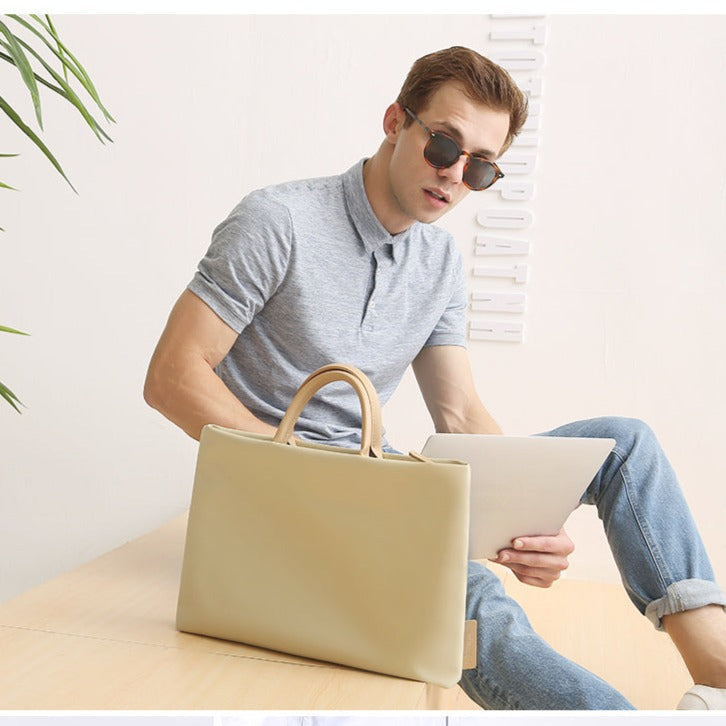 Homme assis tenant une tablette, le sac à main beige pour ordinateur posé devant lui, poignées relevées.